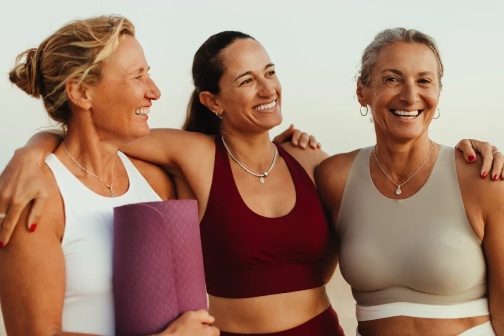 Women in yoga wear standing arm in arm on the beach