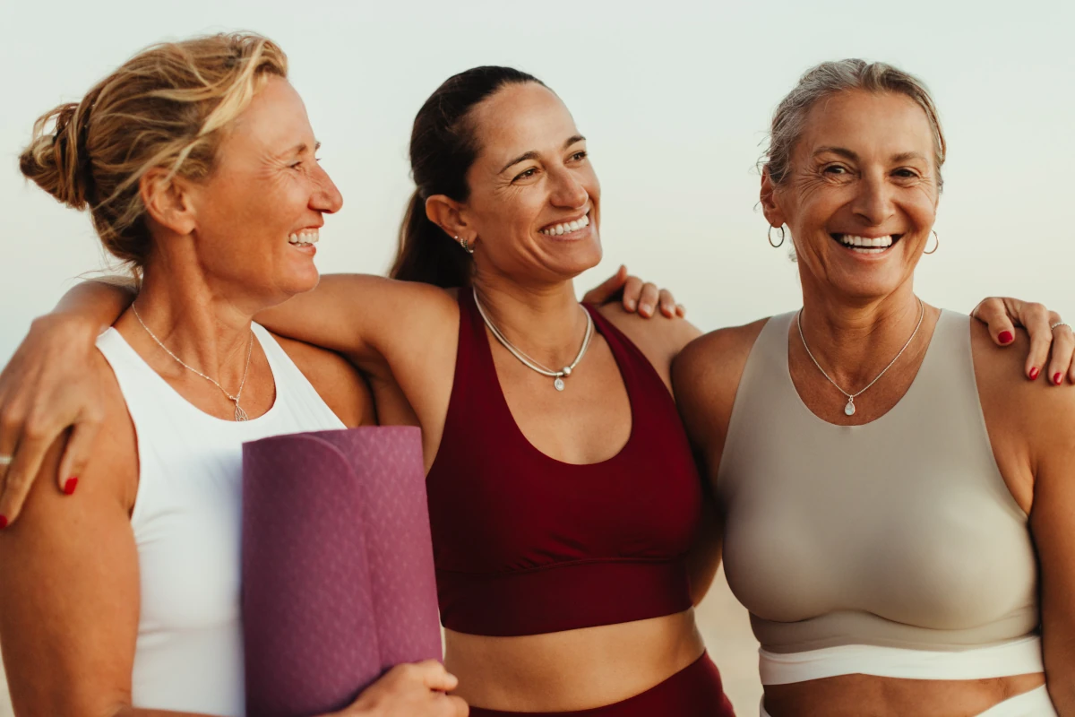 Women in yoga wear standing arm in arm on the beach